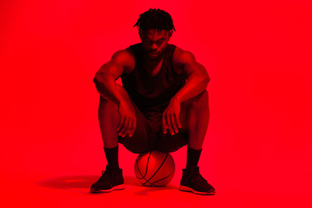 Basketball, break and fitness with man in red filter lighting for challenge, game or performance. Exercise, relax and sports with African person in studio for competition, training or recreationの写真素材