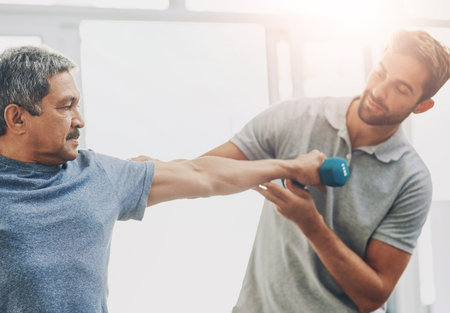 Elderly man, exercise and dumbbell with physiotherapist for rehabilitation, wellness and muscle fitness. Senior person, workout and hand weight for management of pain, arthritis and cardio healthの写真素材