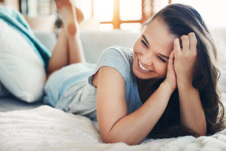 Woman, smile and relax on bed with wellness, morning peace and calm weekend in home. Female person, happy and resting on mattress with vacation break, comfortable and wake up for energy in bedroomの写真素材