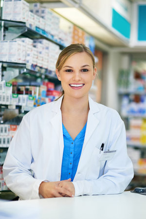 Portrait, pharmacy and woman with smile, counter and healthcare with confidence, pride and medical. Face, person or professional in coat, career ambition or pharmaceutical drugs with friendly serviceの写真素材