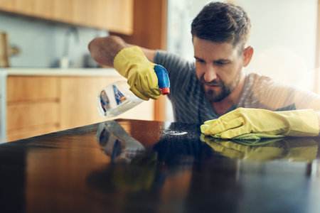 Housekeeping, wipe and man in kitchen in home with cloth and spray detergent for dirt removal. Sanitizing, gloves and male person cleaning table for germs, bacteria or dust at apartment in Canada.の写真素材