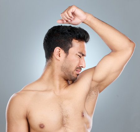 Man, armpit and smell with disgust in studio for unpleasant odor, problem and stink of sweat. Topless, male person and underarm with bad hygiene for foul, scent and hyperhidrosis on gray backgroundの写真素材