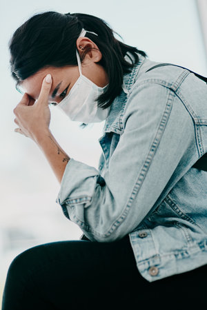 Woman, headache and face mask in clinic for covid, healthcare and waiting room for hospital checkup. Symptoms, fatigue and stress for medical results or wellness, pandemic patient and migraineの写真素材