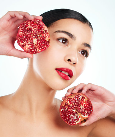 Woman, thinking and pomegranate for beauty in studio, eco friendly skincare and white background. Female person, planning and sustainable lipstick or facial treatment, cosmetics and organic detoxの写真素材