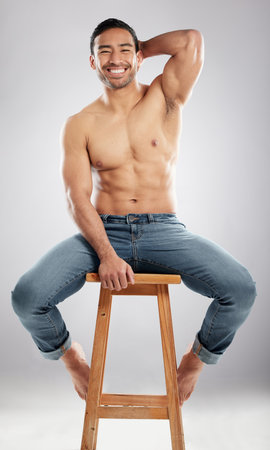 Man, stool and shirtless with muscle in studio portrait with smile, jeans or pride for healthy body. Person, model or bodybuilder with results, wellness and lose weight for change by white backgroundの写真素材