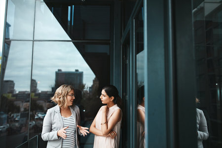 Office, balcony and business women for listening, planning and teamwork with conversation. Workplace, project manager and personal assistant for collaboration, communication and ideas of peopleの写真素材