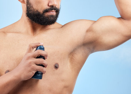 Man, apply deodorant and spray in studio, underarm and grooming cosmetics on blue background. Male person, armpit and fragrance for hygiene treatment, clean smell and antiperspirant for sweatingの写真素材