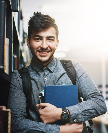University, library and portrait of man with books for knowledge, education or development. Scholarship, student and shelf with study material at campus for literature information, learning or growthの写真素材