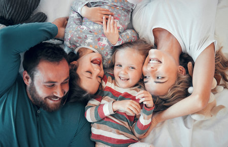 Above, portrait and happy family on bed for love, support and relax together in home. Mom, dad and parents with kids or excited at house, care and protection or morning for children in apartmentの写真素材