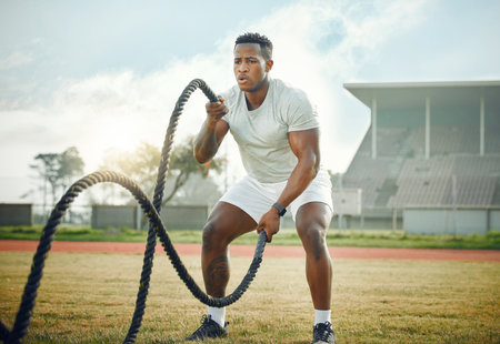 Black man, outdoor and gym with battle ropes, field and fitness for resistance training or exercise. Male person, cardio and routine for bodybuilding, strong muscle and endurance for power or workoutの写真素材
