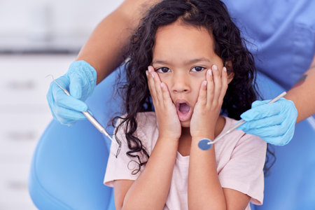 Scared kid, portrait or hands of dentist with tool for dental health, teeth cleaning or cavity treatment for oral hygiene. Pediatric clinic, girl or worried child with fear for medical consultationの写真素材