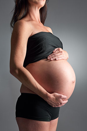 Studio, pregnant and person with hands for stomach, growth and health of baby, body and glow with cosmetics. Grey background, mom and child in belly or abdomen, shine and skincare for parent and skinの写真素材