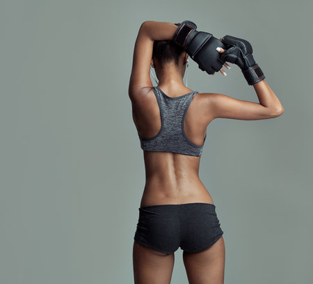Fitness, back and female boxer in studio for sport, ready and training on gray background. Workout, woman and stretching for exercise with sportswear, boxing gloves and earphones for determinationの写真素材