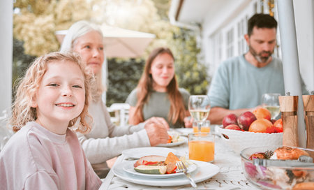 Kid, portrait and family with lunch outdoor for holiday celebration, brunch or eating food with bonding. Girl child, people and dinner event on patio in festive season with relax, nutrition or happyの写真素材