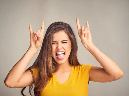 Woman, portrait and devil horns with hands in studio for grunge sign, tongue out or rock gesture on...