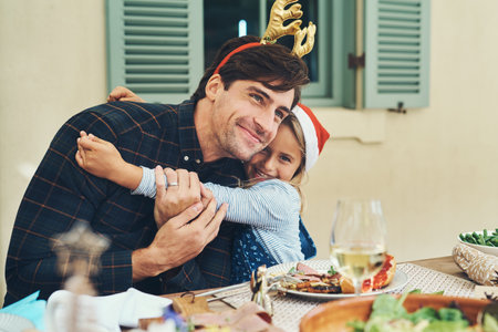 Christmas, dad and child at table with hug, bonding and happy family celebration together for lunch. Smile, father and daughter embrace at festive holiday event with food, love and fun xmas in homeの写真素材