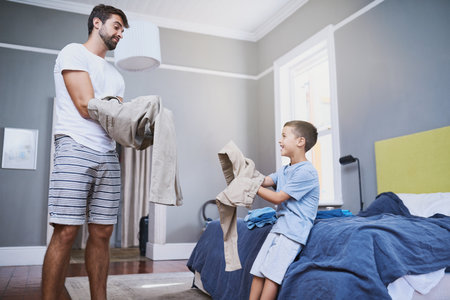 Morning, father and child dressing in bedroom for preparation, routine or getting ready on weekend. Clothes, pants and man teaching young kid for learning, growth development or support in homeの写真素材