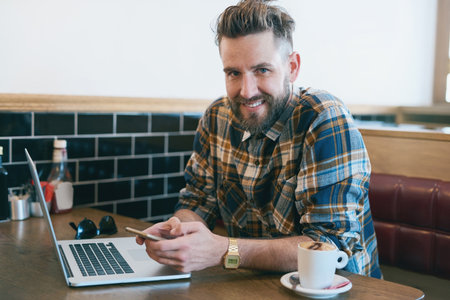 Coffee shop, phone and portrait of man with laptop and drink, caffeine beverage and latte. Restaurant, cafeteria and person on smartphone and computer for social media, remote work and networkingの写真素材