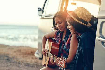 Van, road trip and women at a beach with guitar for sunset, adventure and music while bonding on vacation in nature. Caravan, travel or friends at sea with acoustic instrument, song or fun in Mexicoの写真素材
