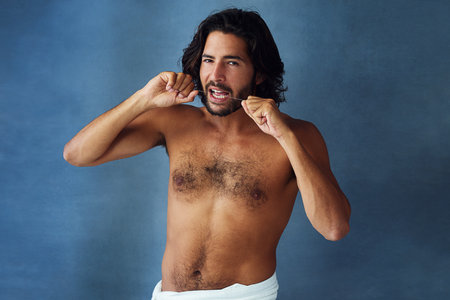 Portrait, man and flossing teeth in morning routine for wellness, cavity and dental hygiene on blue background. Male person, cosmetic and oral product for healthy mouth, confidence or pride in studioの写真素材
