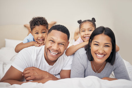 Morning, family and children with portrait on bed for bonding, connection or relax together in bedroom. Parents, young kids and happy man with woman playing for love, hug or care in home on weekendの写真素材