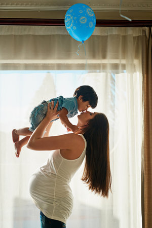 Pregnancy, balloon and mom with child kiss for bonding, loving relationship and support by window....