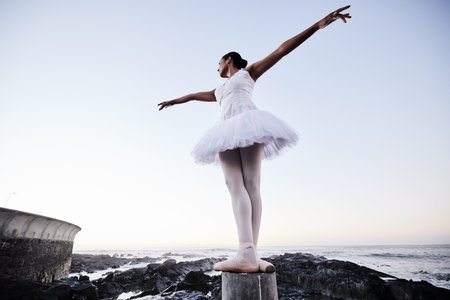 Girl, ballet and stretching at beach for dance for freedom, peace and creative performance with balance. Woman, ballerina and moving outdoor at ocean for aesthetic, fitness or training with low angleの写真素材