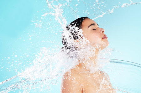 Cleaning, hygiene and water splash with woman in studio on blue background for skincare. Beauty,...