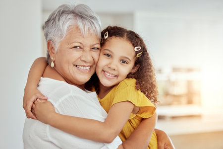 Hugging, sofa and portrait of child with grandmother for love, care and bonding together in home. Smile, connection and girl kid embracing senior woman for relax in living room at house in Colombia.の写真素材