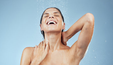 Happy, woman and shower water in blue background for skincare, wellness and hygiene with eyes closed in hair care. Female person, excited and fresh for cosmetics in studio, morning routine and beautyの写真素材