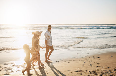 Happy family, walking and holding hands with children on beach sunset for summer holiday or bonding together in nature. Mother, father and kids with smile for stroll or outdoor weekend by sand shoreの写真素材