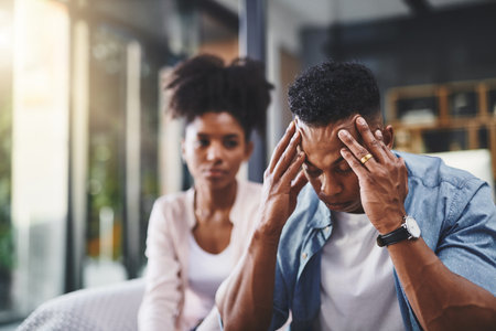 Couple, man and headache from stress with conflict for cheating, betrayal and affair with fight or breakup in home. Black people, migraine and toxic marriage in lounge with disagreement and argumentの写真素材
