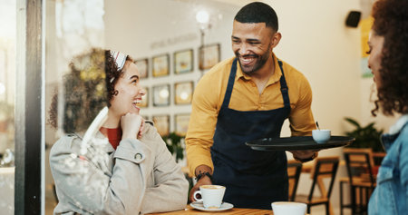 Cafe, women and waiter with coffee order, conversation and customer service at restaurant. Barista, staff and happy girl friends with smile and chat at diner with employee helping with hot drinkの写真素材