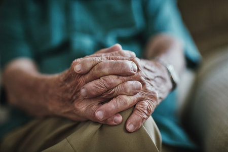 Senior man, hands together and care with support for old age on sofa in retirement home. Closeup of elderly, retired pensioner or male person with pain, grief or loss in recovery or rehab at houseの写真素材