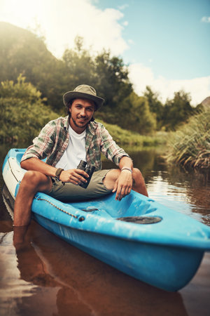 Portrait, canoe and man with adventure, explore and tourism with binoculars, journey and relax. Face, person and traveller with nature, stress relief or vacation with getaway trip, sightseeing or joyの写真素材