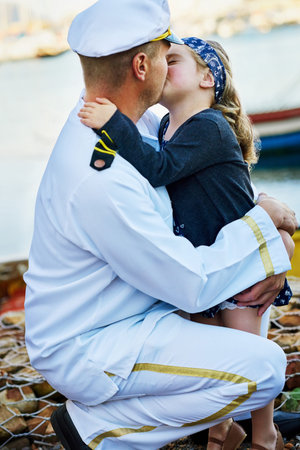 Navy, father and young child with kiss for reunion, love and welcome by dock on seaside. Male...