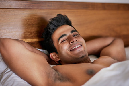 Man, bed and portrait with waking up happy from rest with comfort in house, shirtless and morning. Confidence, relax and lazy on weekend with pride for break with sleeping in, alone and comfortableの写真素材