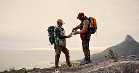 Hiking, friends and men on mountain with drink for adventure, exercise and fitness. Travel, nature and happy people outdoors for wellness, coffee and trekking on holiday, backpacking or vacationの写真素材