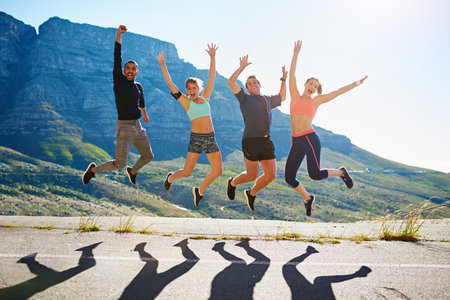 Jump, friends and portrait of people on road in city for workout, exercise and marathon training outdoors. Sports, fitness and men and women for challenge, cardio and performance for running togetherの写真素材