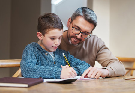 Help, homework and dad with child at desk for teaching, learning and notebook for school project. Writing, notes and father studying in home with son for support, advice and growth in kids educationの写真素材
