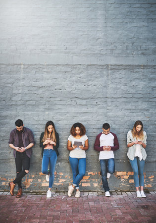 People, row and online outdoor with technology for study break, social media and campus friends. College, students and wall background with texting for communication, digital interaction and search.の写真素材
