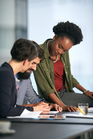 Woman, coaching and meeting with team for training staff, collaboration or assistance at office. Female person or employee helping colleagues with paperwork or documents for review or ideasの写真素材