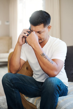 Stress, man and talking with phone at house couch for argument, mistake problem and communication crisis. Frustrated, male person and mobile discussion, bad news and conflict online with connectionの写真素材