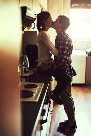 Home, happy couple and kiss for relationship with care, support and romantic connection for anniversary. Man, woman and intimacy with love together for healthy marriage and soulmate bond in kitchenの写真素材