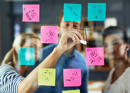 Business, hand or brainstorming with sticky notes on glass for planning sales project, strategy process or tasks. Collaboration, writing and employees in meeting for ideas, solution or goals scheduleの写真素材