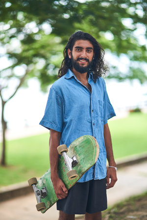 Indian man, nature and skateboard for portrait, smile and balance sport or hobby in park. Workout, trees and male person for adventure and skater, alone and exercise for freedom and adrenalineの写真素材