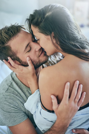 Love, kiss and intimate couple in bed with romance, affection and morning bonding in apartment. Relationship, man and woman relax in bedroom with happy embrace, passion and care on weekend in homeの写真素材