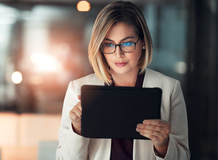Corporate woman, tablet and working at night in office for company agenda, research and planning. Executive, technology and reading email or report for business results, growth and revenue with dataの写真素材