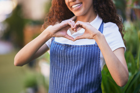 Hands, woman and waitress with heart shape outdoor for career in hospitality industry by cafe. Smile, pride and female barista with apron for coffee shop with love emoji, sign or gesture in nature.の写真素材