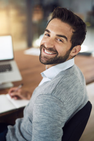 Laptop, portrait and man at desk with notes, pride and business plan at digital agency with smile. Confidence, tech and happy businessman in office with report, online research or project managementの写真素材